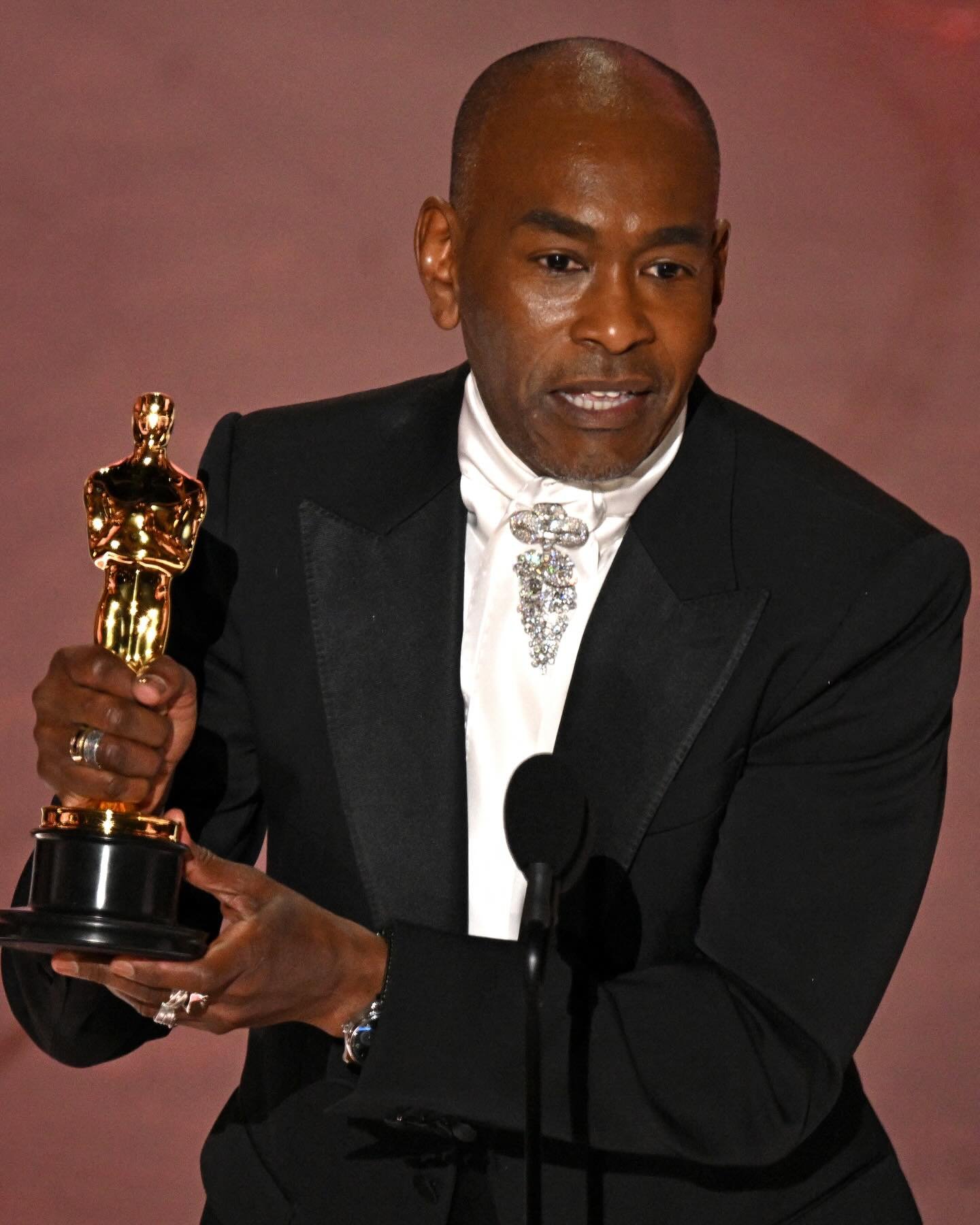 Pessoa segura uma estatueta do Oscar, destacando-se em evento elegante. Enfatiza os melhores momentos do Oscar 2025.