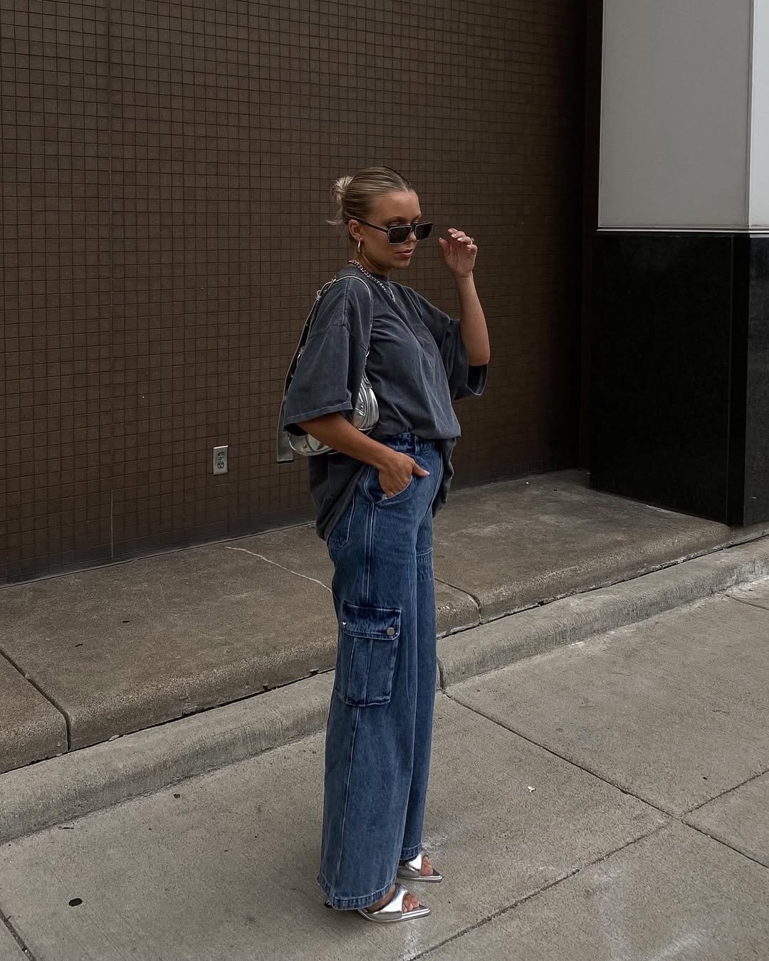 Mulher usando óculos escuros, camiseta larga e calça jeans cargo. Estilo casual em cenário urbano.