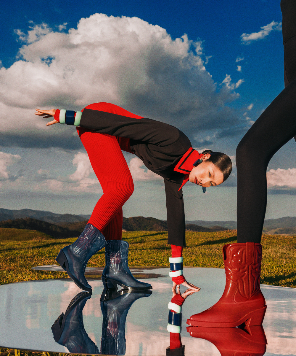 Pessoas em pose artística ao ar livre, usando botas estilosas, refletidas no espelho no chão.