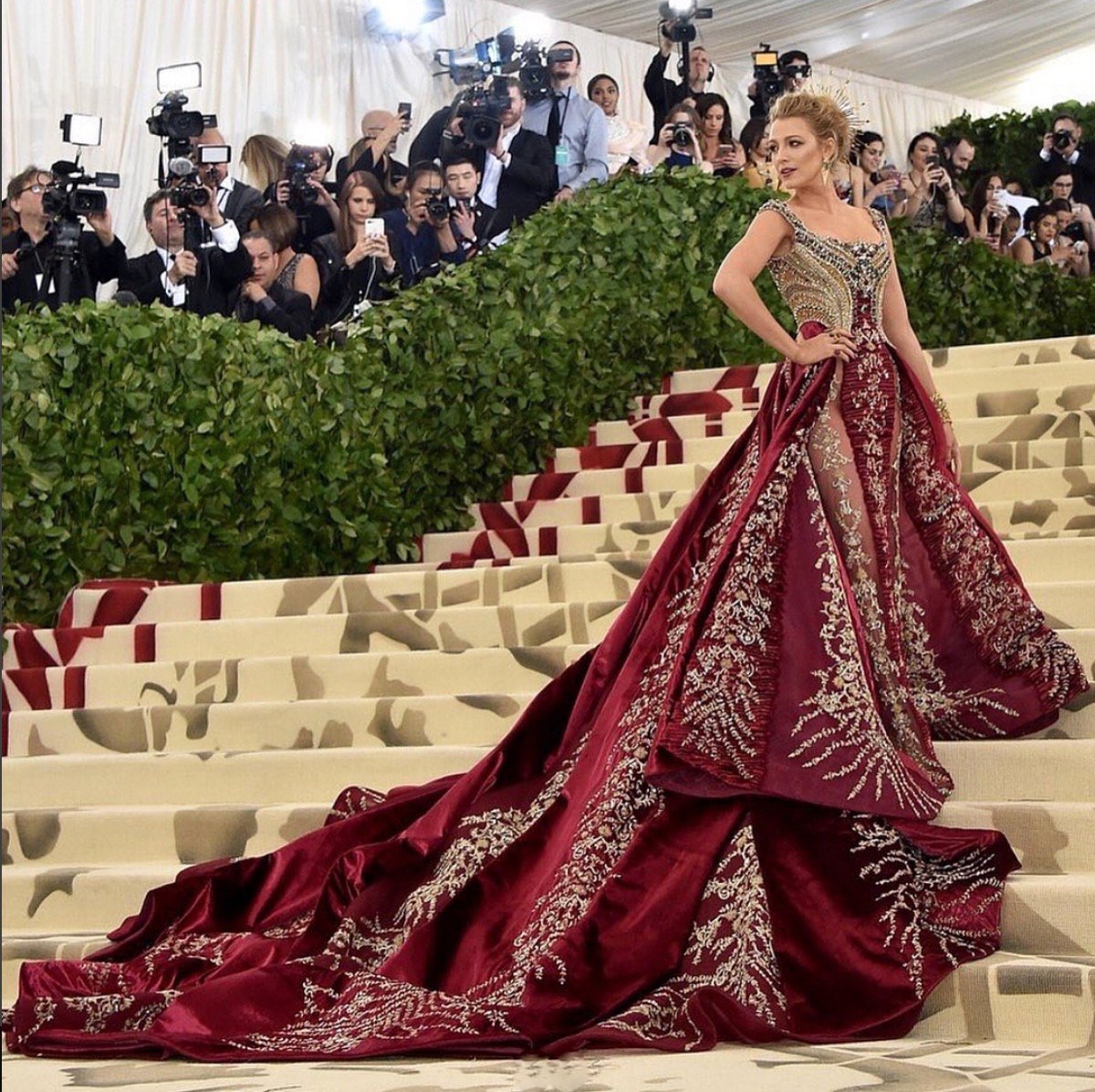 Uma mulher em escadarias luxuosas, vestida com longo vestido vermelho bordado.