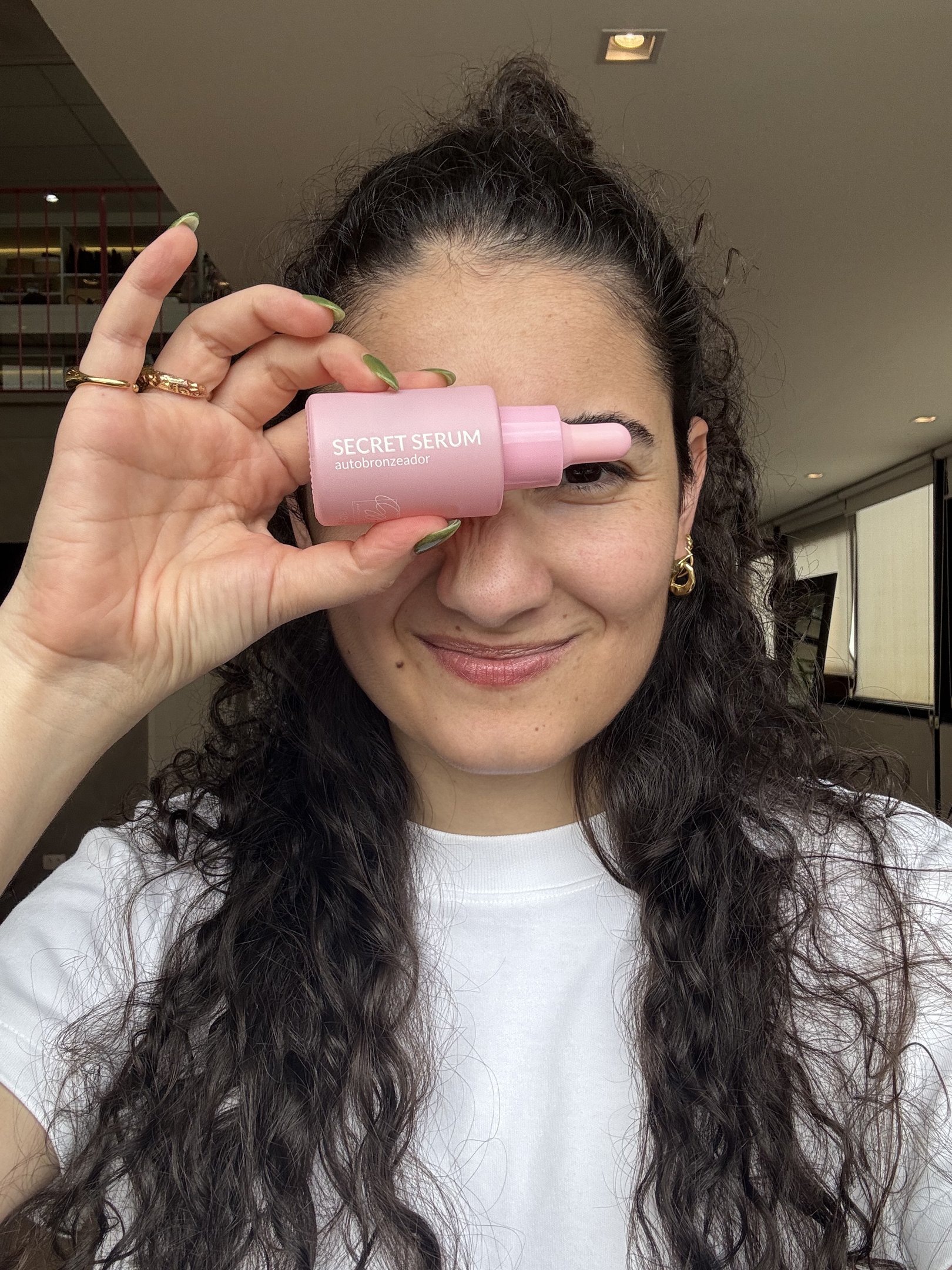 Mulher sorrindo segura frasco de autobronzeador rosa, destacando produto para pele bronzeada.