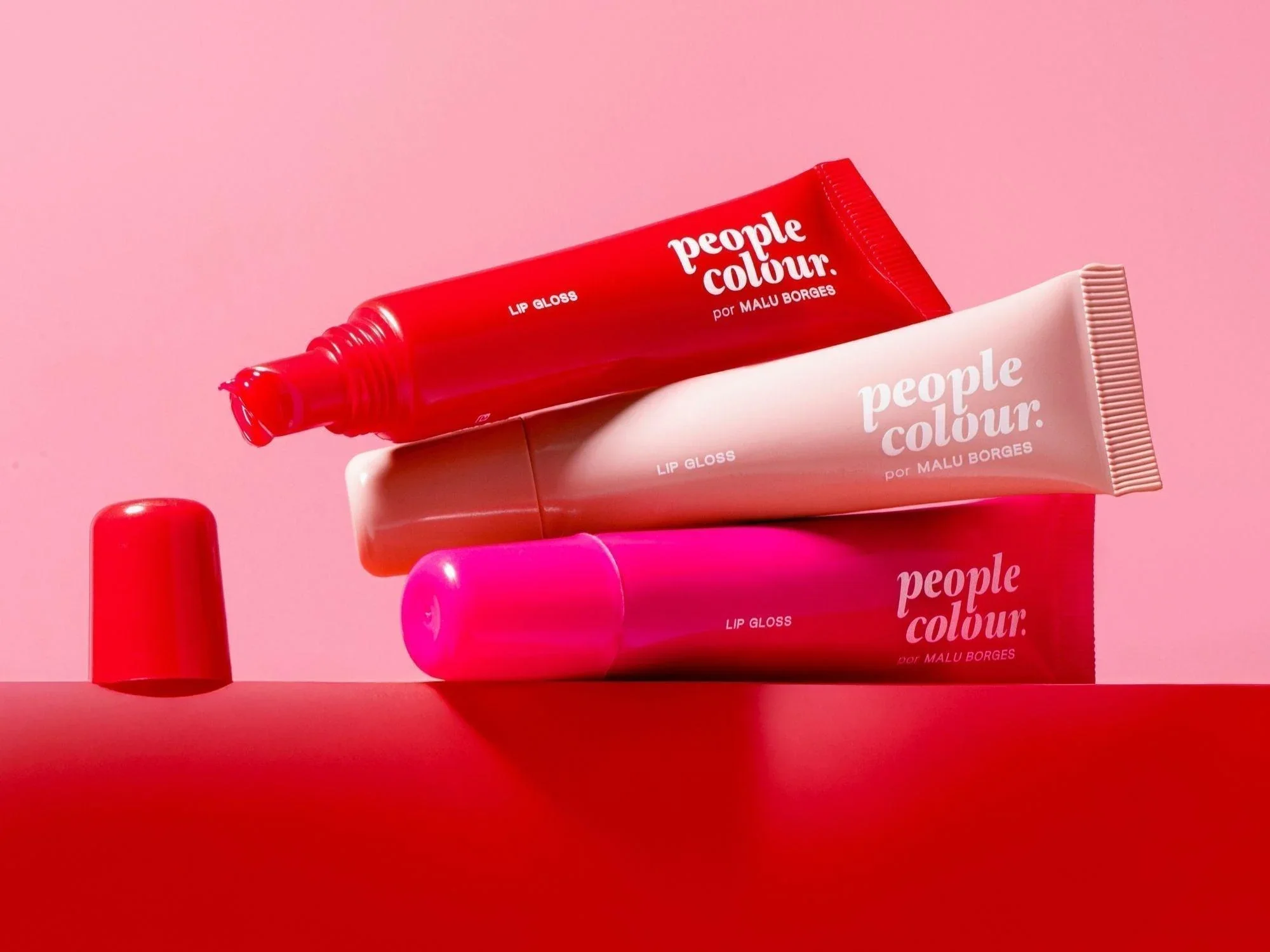 Três tubos de gloss labial em tons rosa e vermelho, com rótulos
