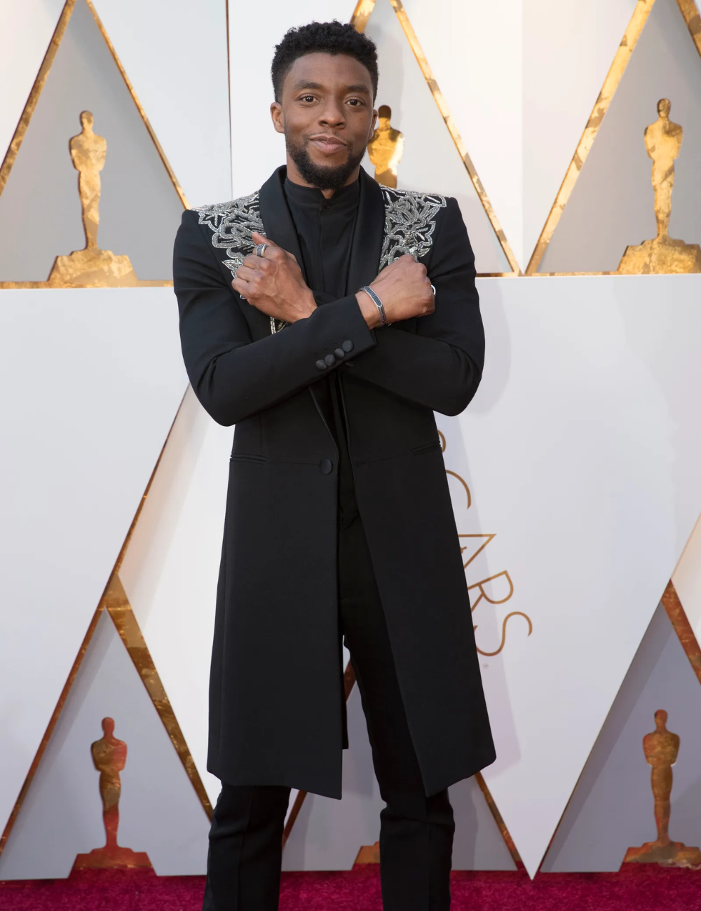 Um homem posando em um tapete vermelho com um terno preto estiloso.