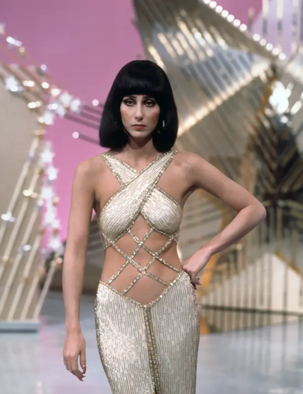 Vestido glamouroso dourado com recortes geométricos, representando referências na moda elegante e sofisticada. Fundo decorativo.