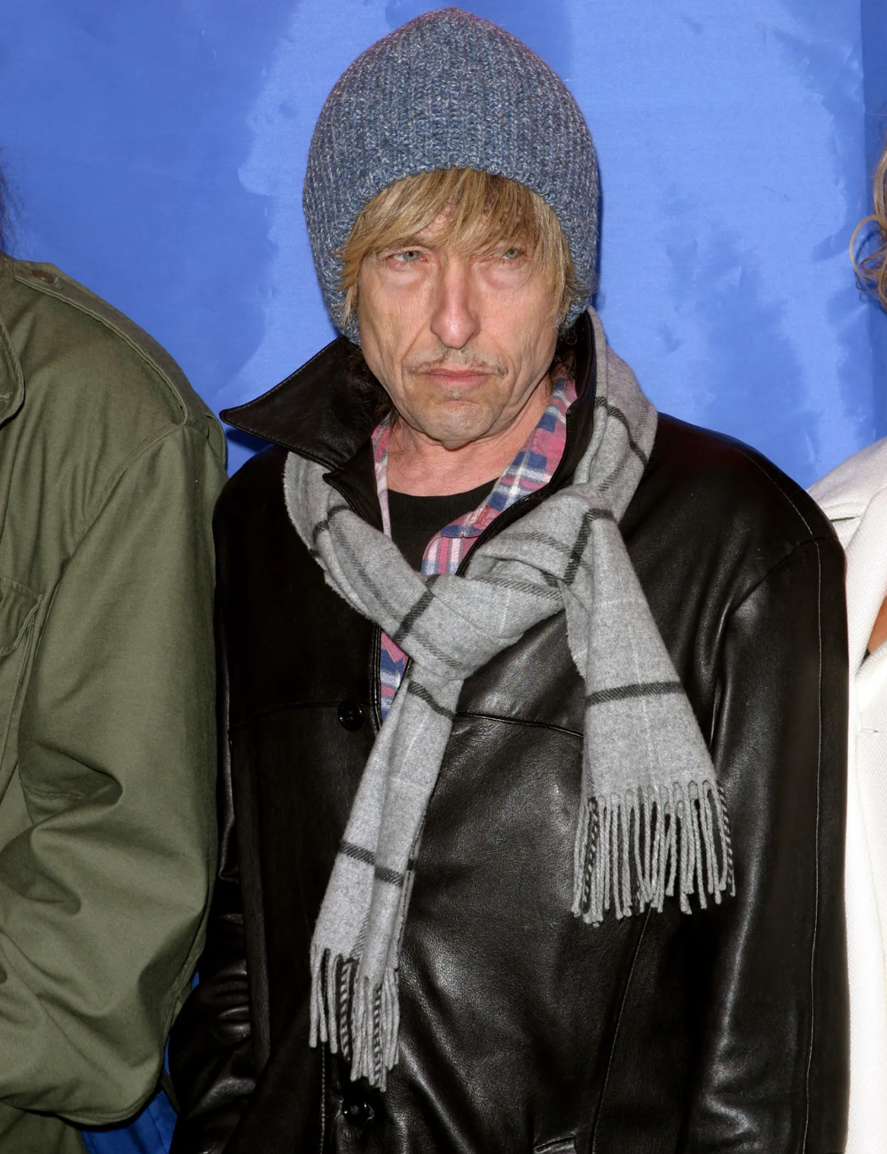 Pessoa com gorro cinza, cachecol listrado e casaco de couro preto. Estilo casual e influências de moda.