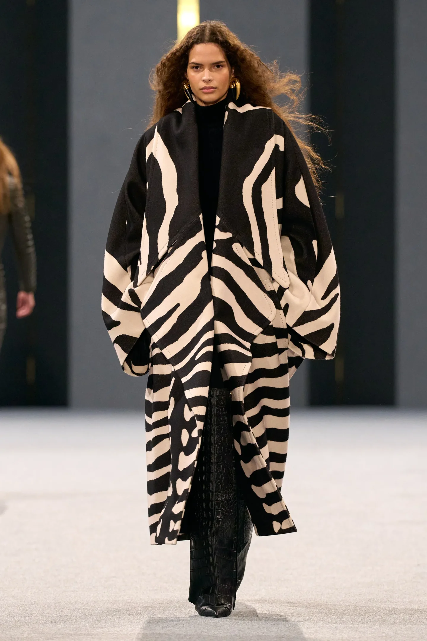 Modelo veste casaco com estampa zebrada preto e branco em desfile, destacando a moda temporada Outono/Inverno 25.