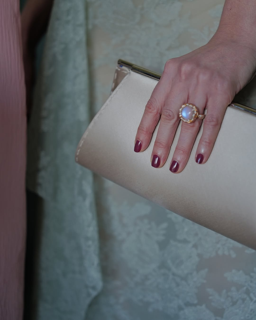Mão segurando uma clutch dourada, unhas das celebridades pintadas de vermelho escuro e com anel de pedra clara.