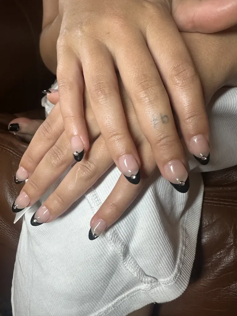 Unhas decoradas com esmalte nude e francesinha preta, adornadas com minúsculas pedrinhas brilhantes.