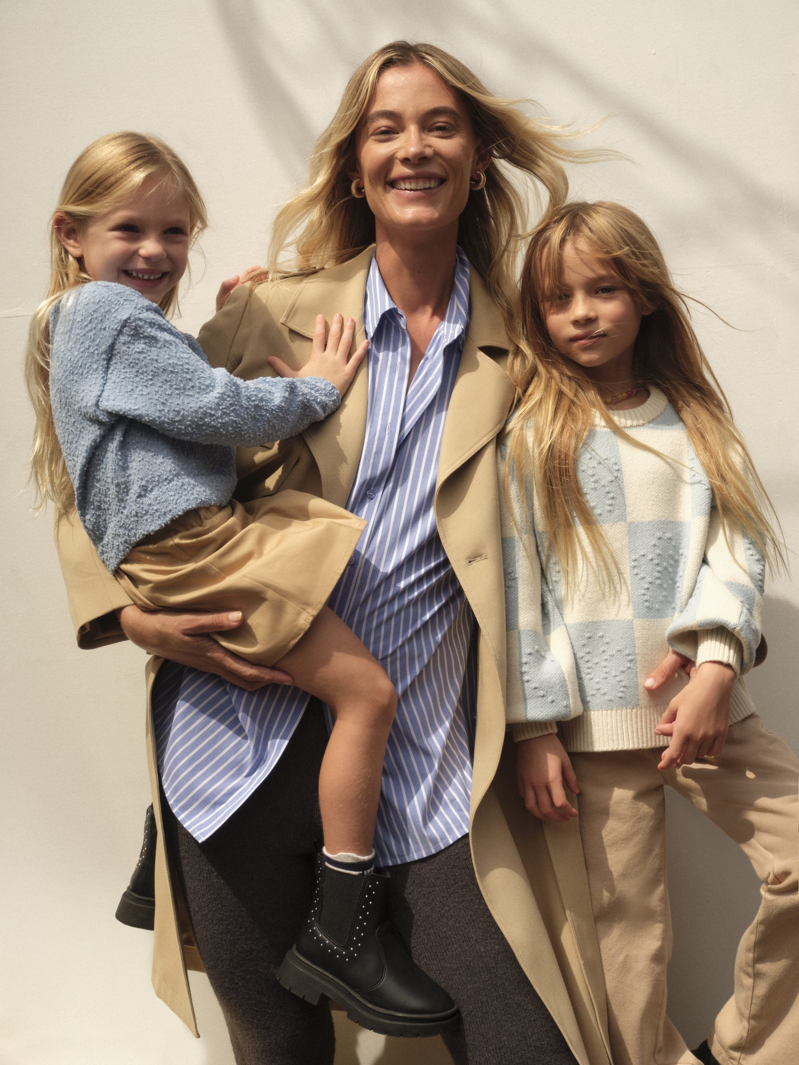 mãe com filhas sorrindo para a foto vestindo peças versáteis de inverno como trench coat e camisa 