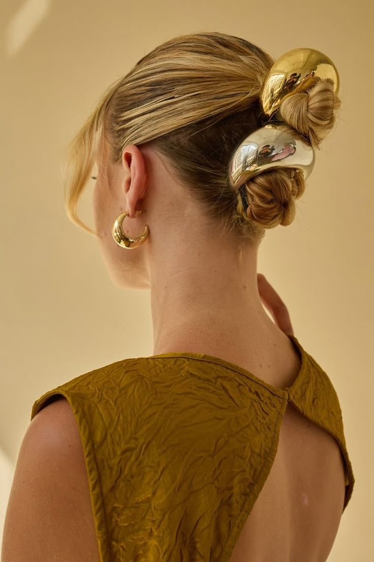 Penteado com coque decorado com acessórios de cabelo chunky dourados, cabelo loiro. Brinco pendente ouro.