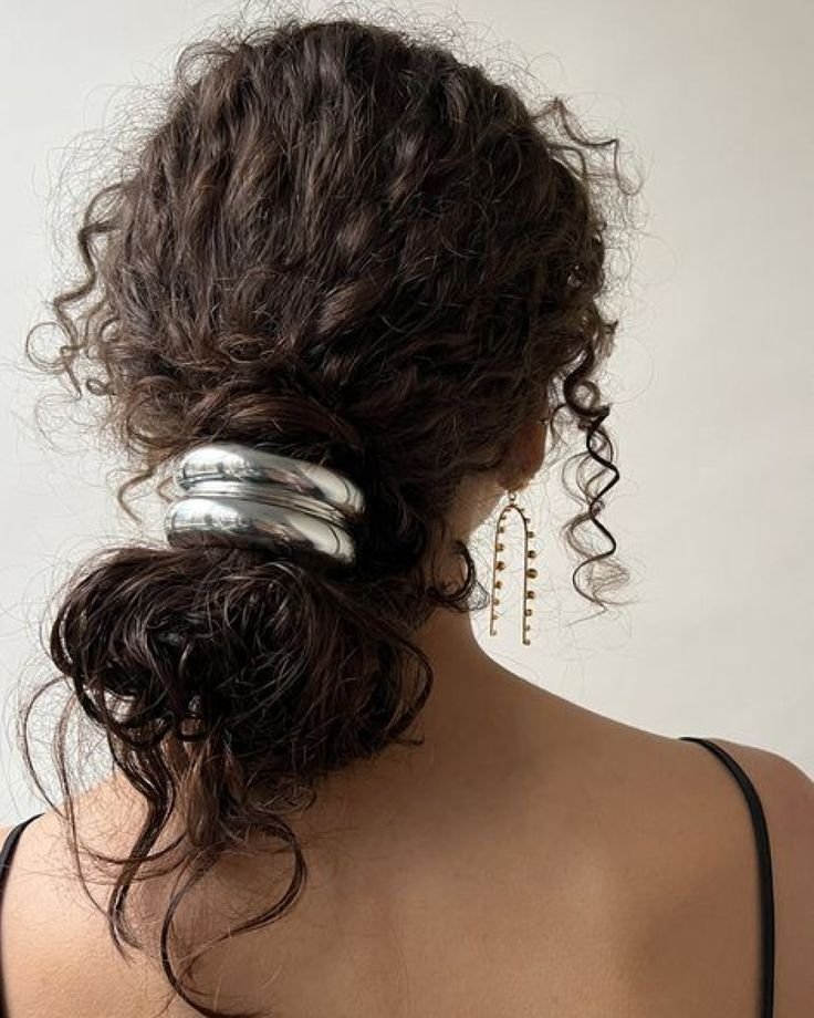 Cabelo cacheado preso com acessório de cabelo chunky prateado, destacando brinco dourado longo.