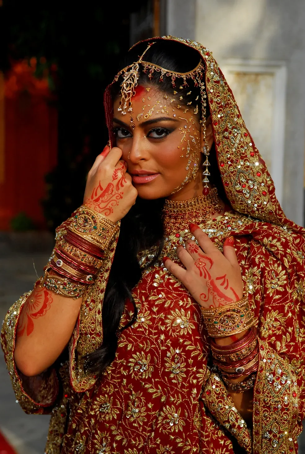 Vestida com roupas tradicionais e joias elaboradas, mulher com adornos detalhados nas mãos, evocando cenários típicos de novelas.