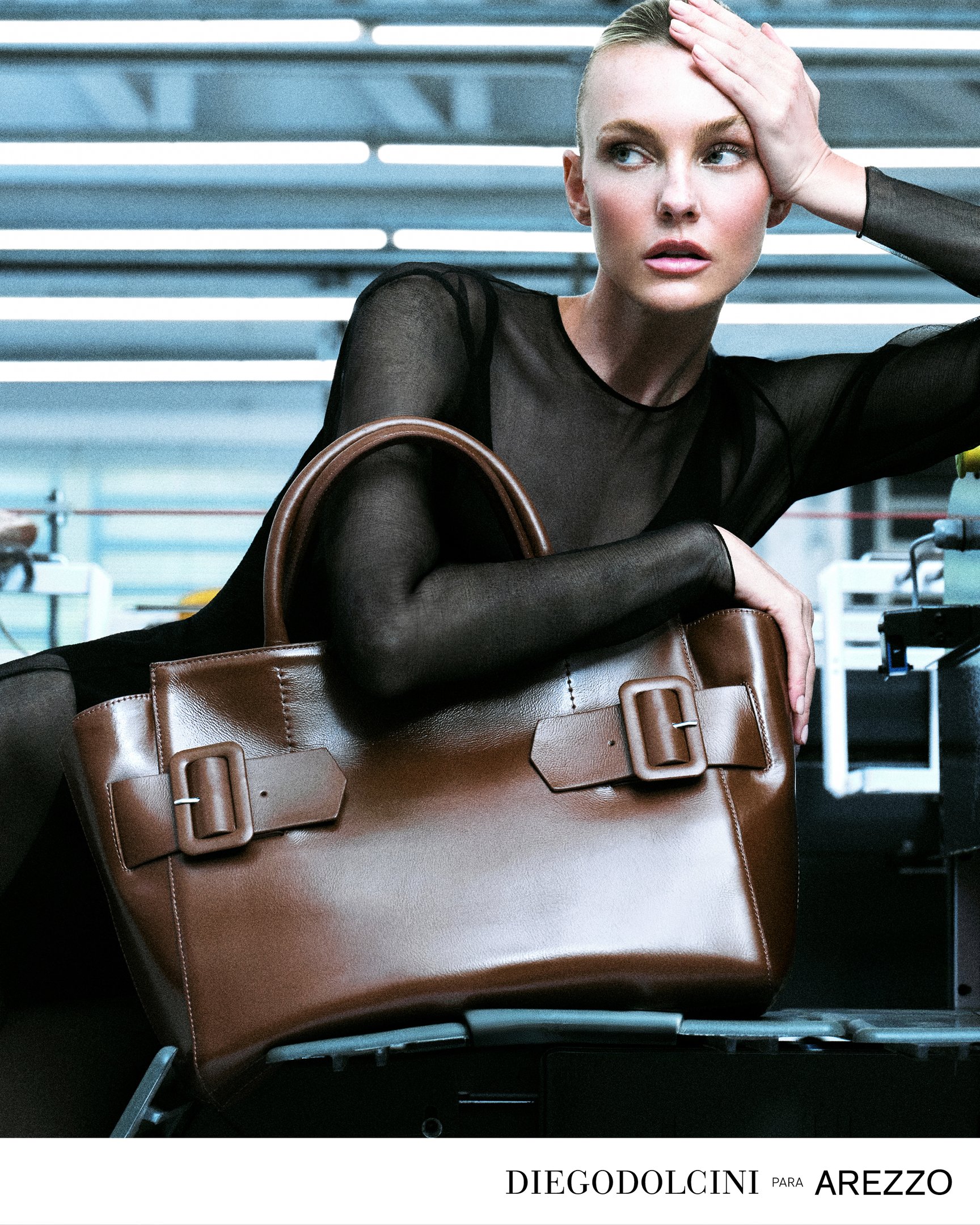 Modelo posa com bolsa marrom collab Diego Dolcini para Arezzo, em ambiente moderno.
