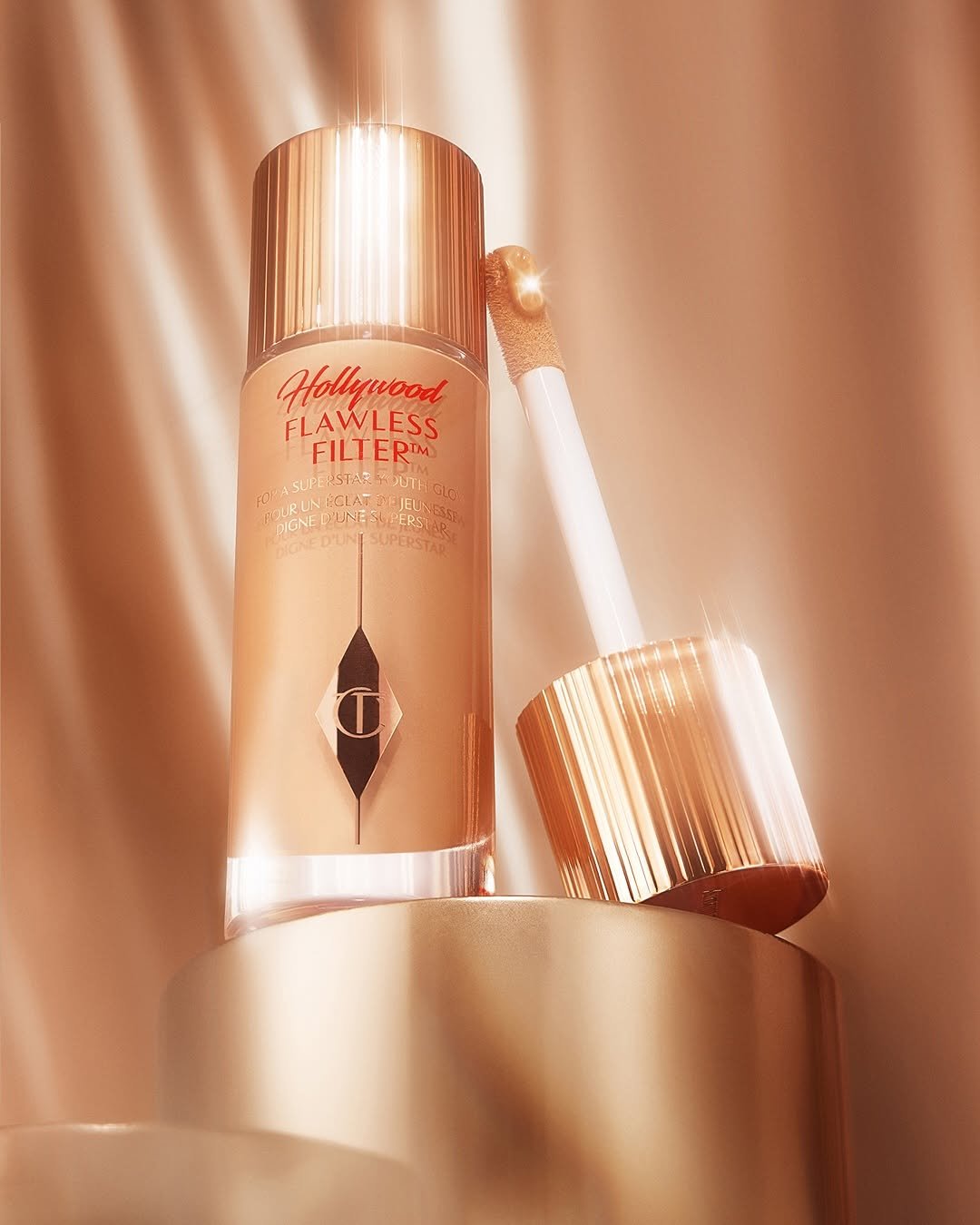 Frasco de maquiagem cintilante com aplicador, refletindo iluminação dourada de fundo. Dupes de beleza.