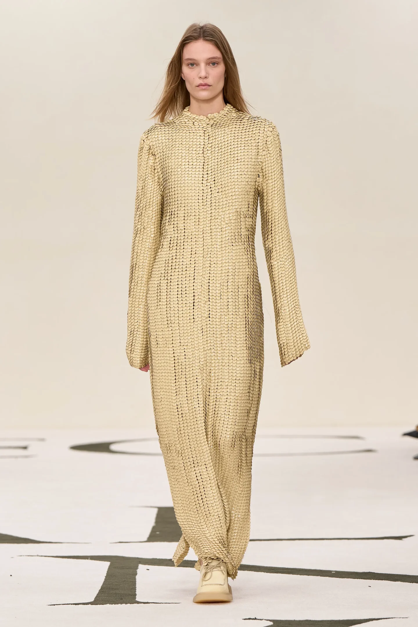 Modelo vestindo traje dourado com textura de cota de malha em passarela.
