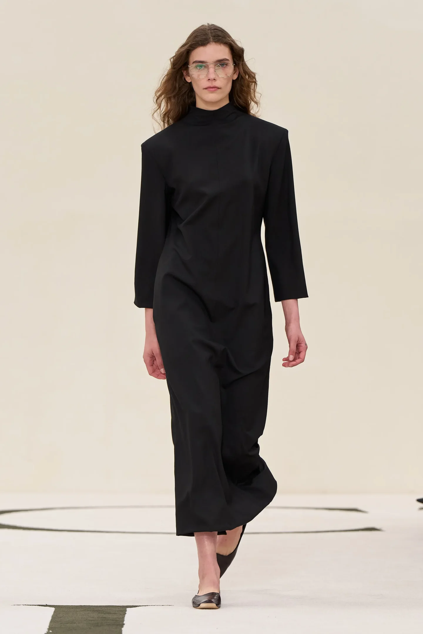 Modelo desfilando com vestido preto de manga longa, estilo minimalista e discreto. Visual conservador
