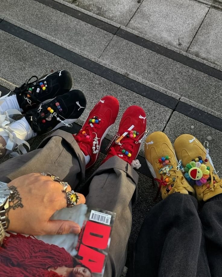 Três pares de tênis coloridos com charms, em tons de preto, vermelho e amarelo, adornados com pingentes vibrantes.