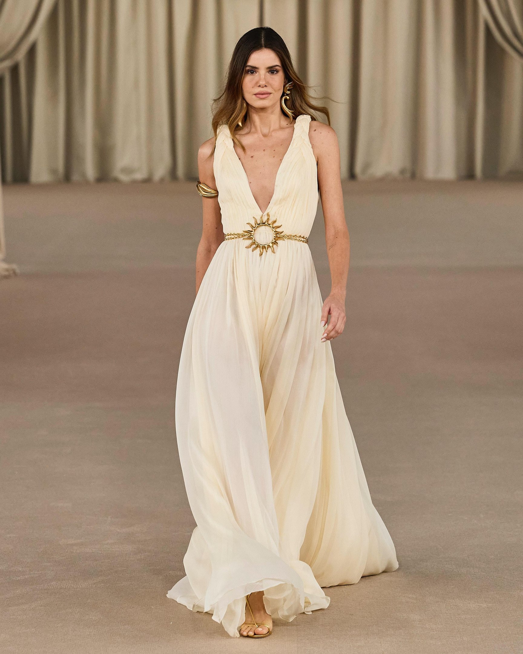 Camila Queiroz desfila usando vestido fluido com detalhes dourados, alinhado às tendências modernas para o verão.