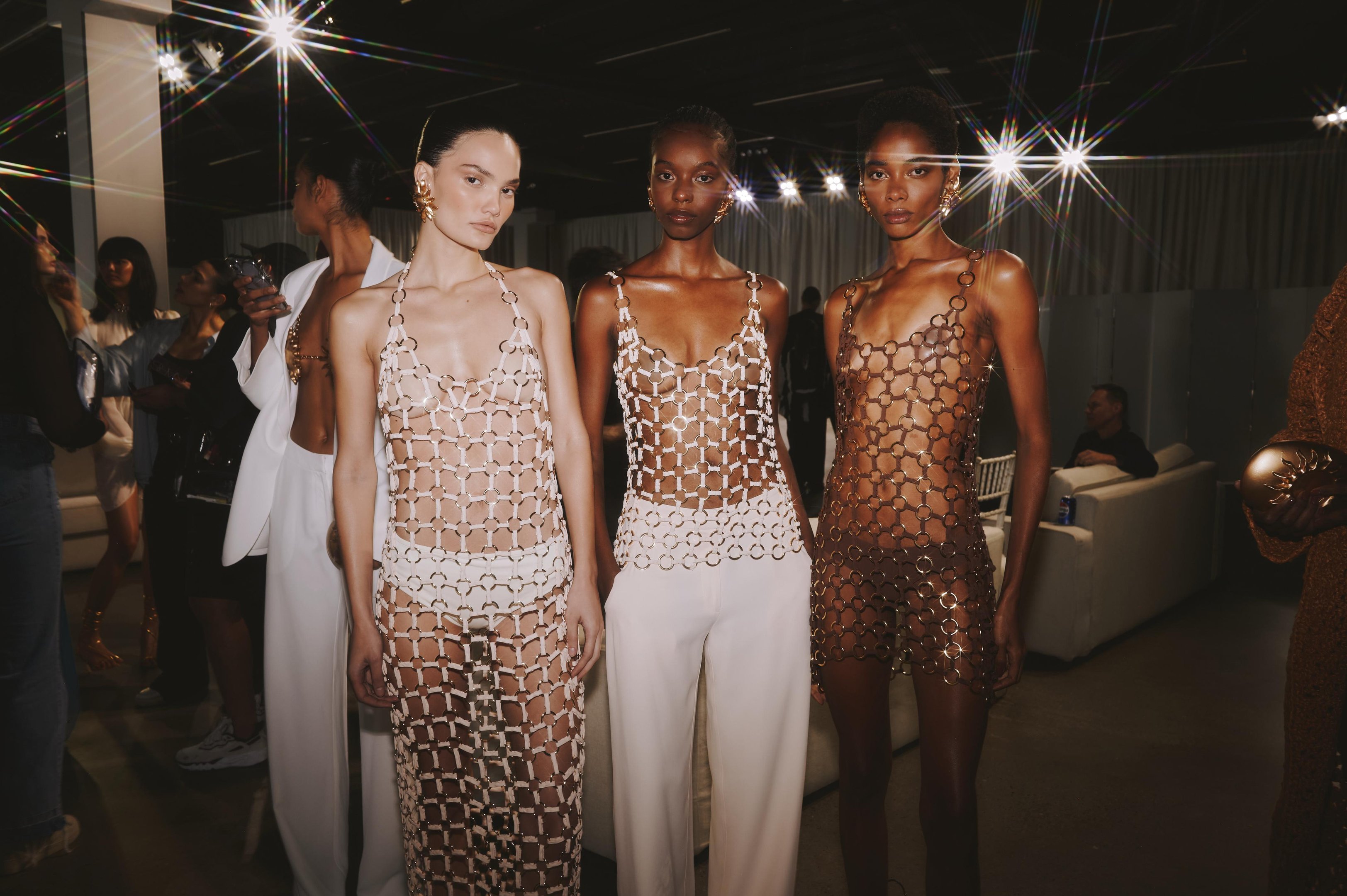 Modelos vestem peças transparentes de correntes, refletindo as tendências de verão em um ambiente sofisticado.
