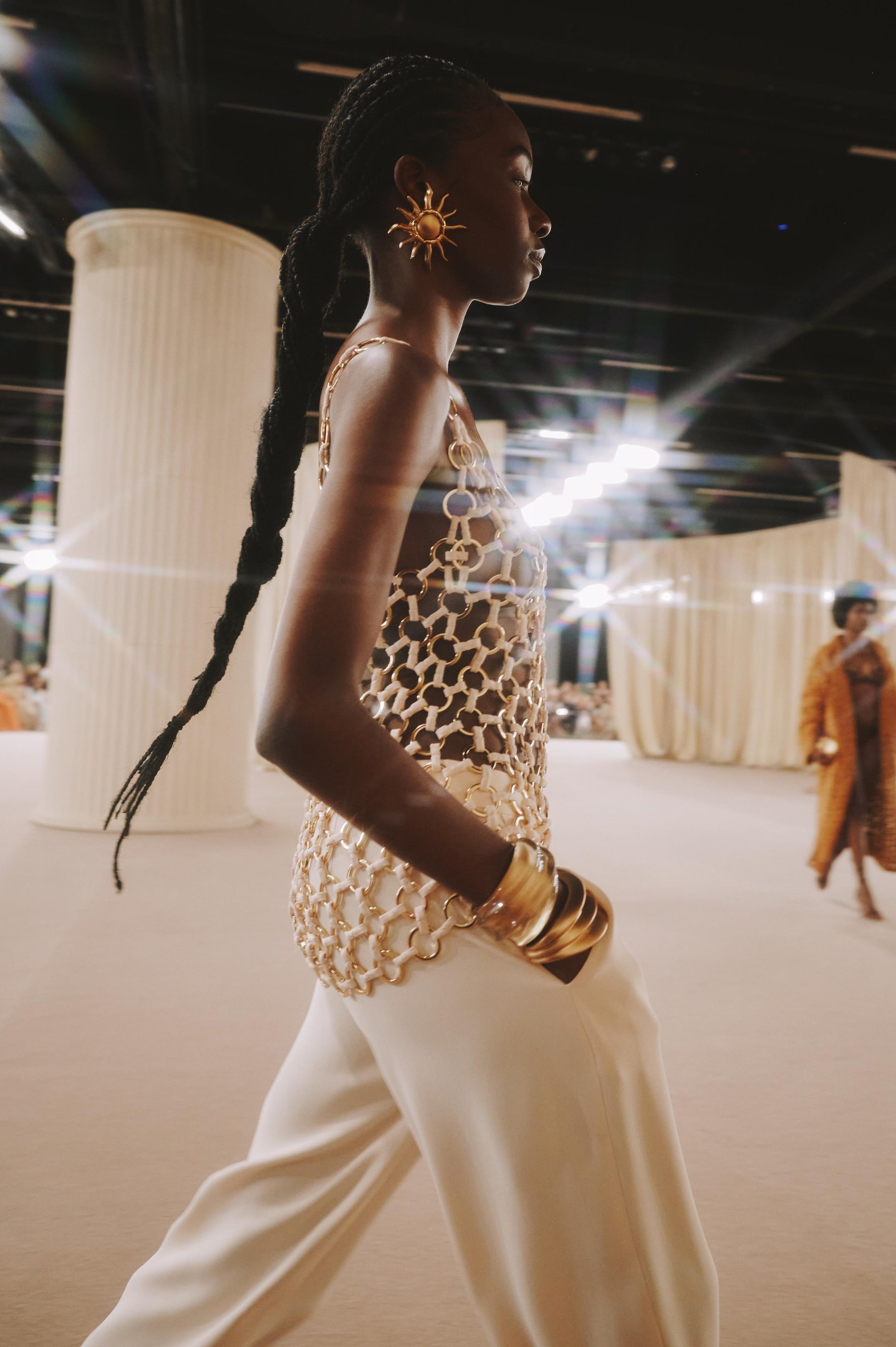 Modelo em passarela usando top dourado e calça clara, representando tendências de verão sofisticadas.