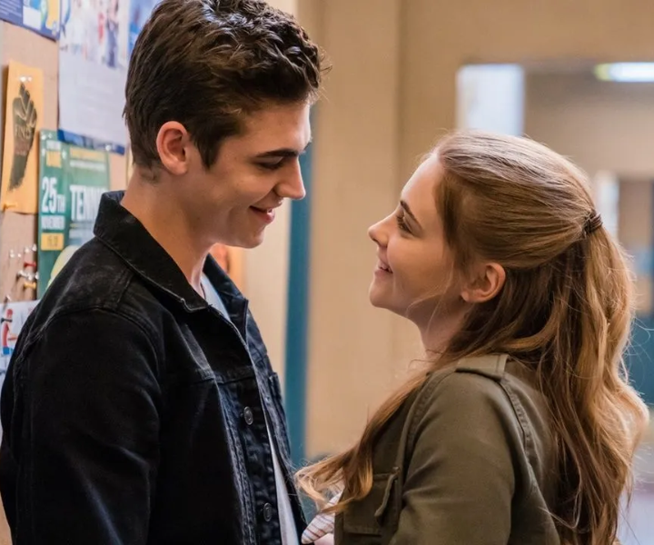 Jovens sorrindo um para o outro em um corredor, cenário típico de fanfics românticas.