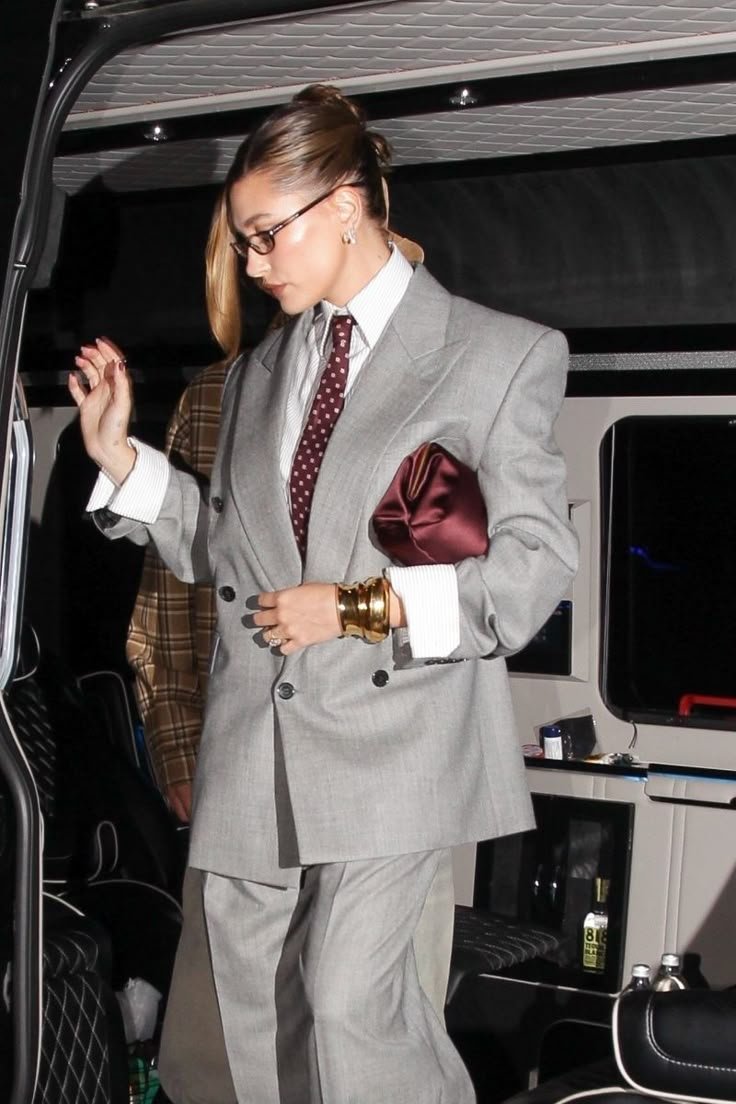 Pessoa usando terninho cinza com gravata vermelha e segurando uma clutch vinho, em ambiente interno.