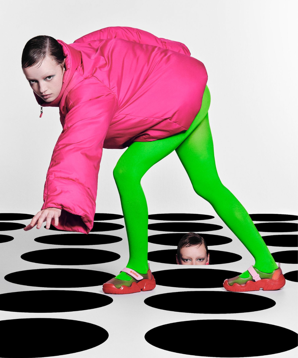 Pessoa em casaco rosa e leggings verdes em ambiente geométrico. Elemento das novidades de moda.