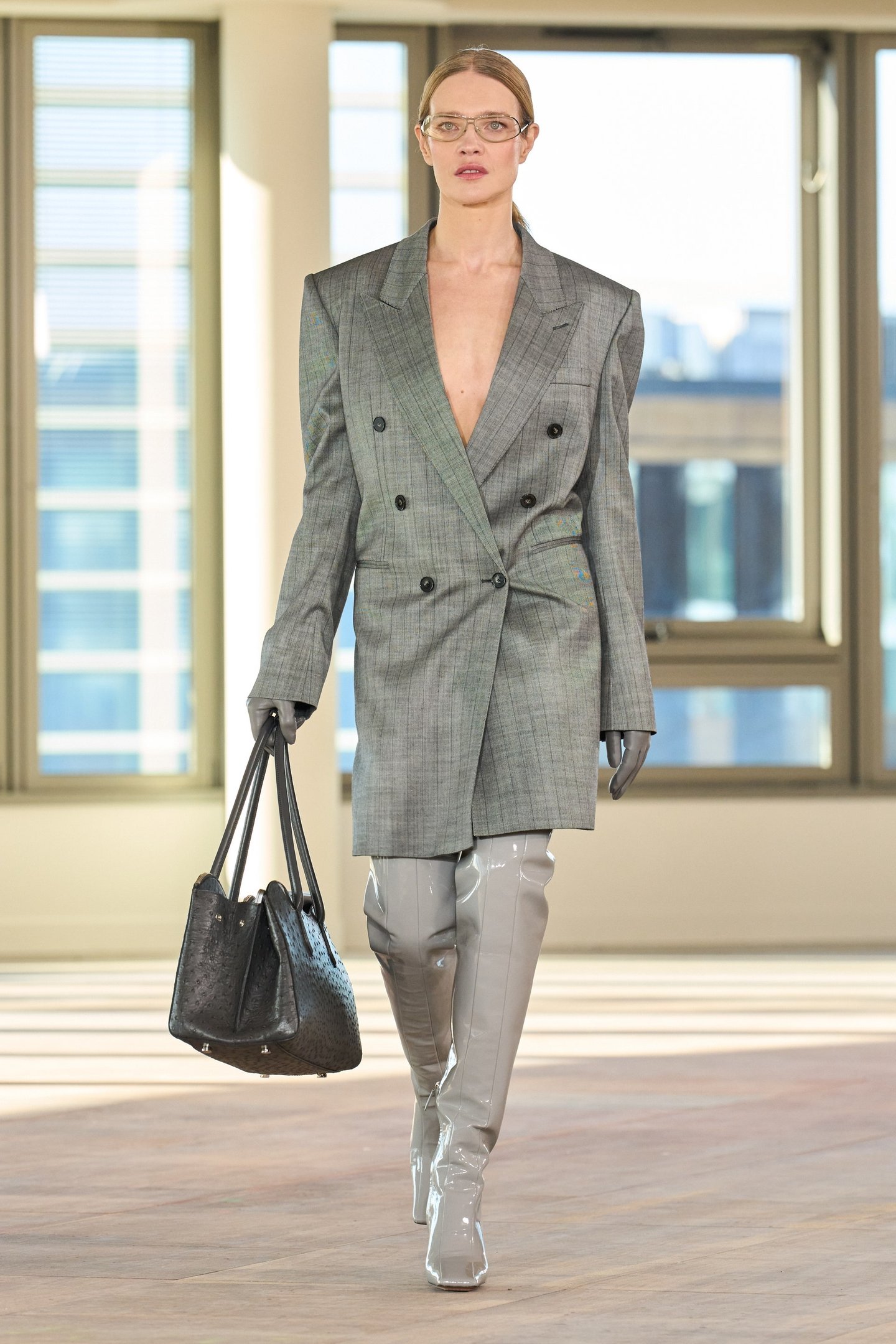 Modelo em passarela veste blazer xadrez e botas cinza over the knee, segurando bolsa preta.