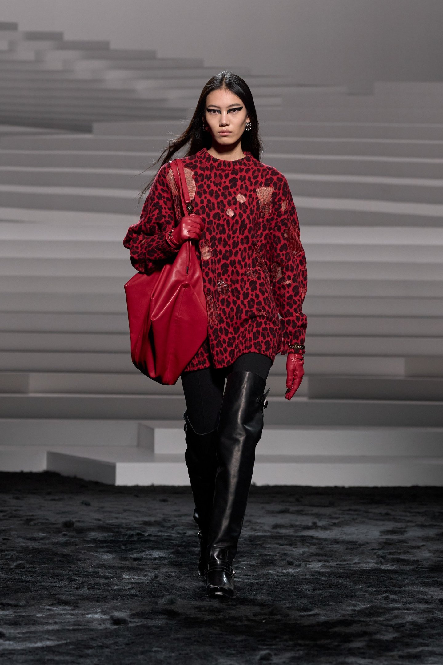 Modelo usando suéter vermelho com estampa de leopardo, calça e bota over the knee preta, bolsa combinando.