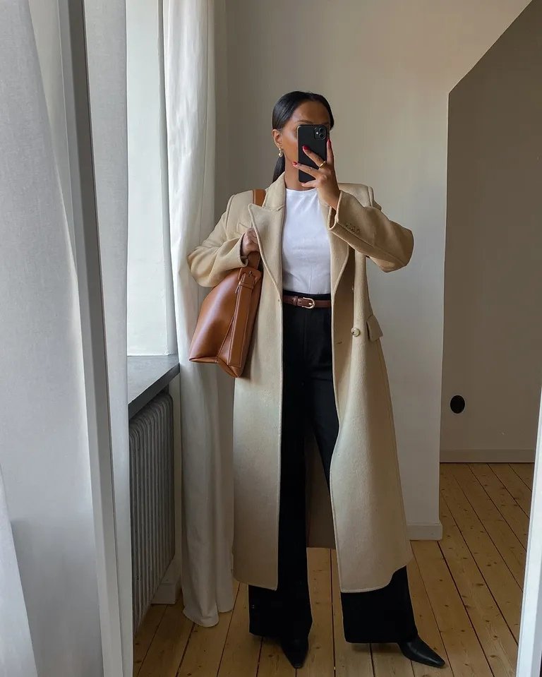 Usuária com casaco bege, calça wide leg preta, bolsa marrom e blusa branca.