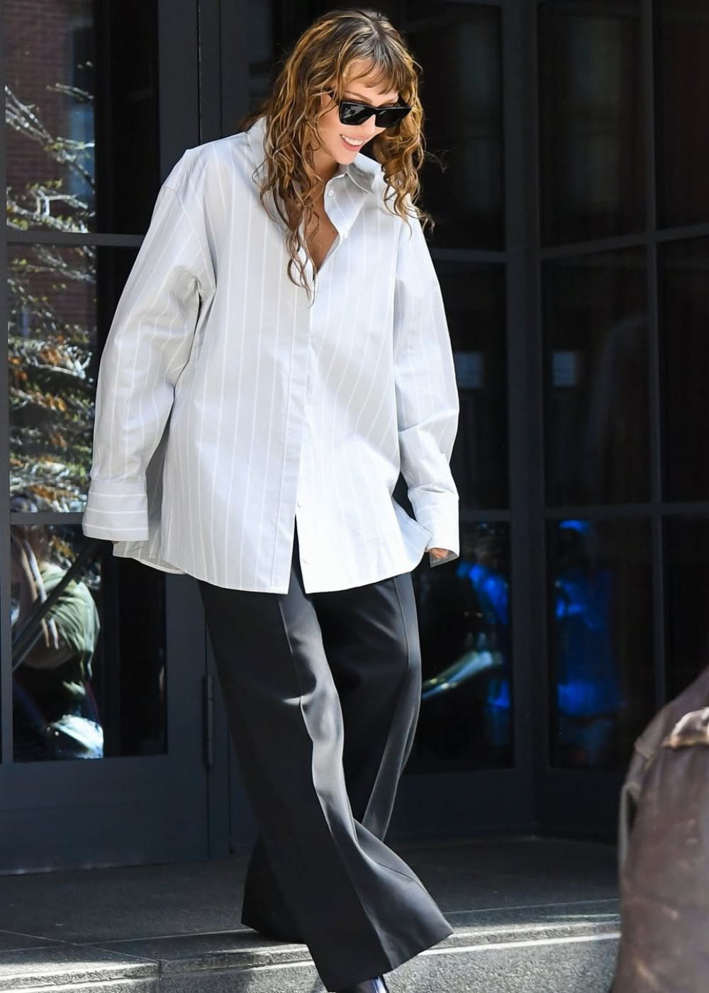 Celebridade com camisa branca larga e calça preta, exibindo casualidade e estilo moderno.