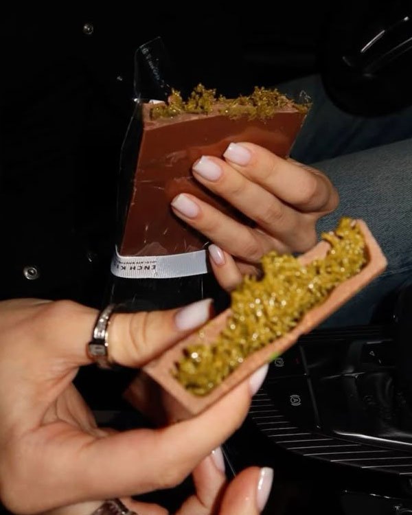 Mãos seguram barras com cobertura verde em chocolate de Dubai.