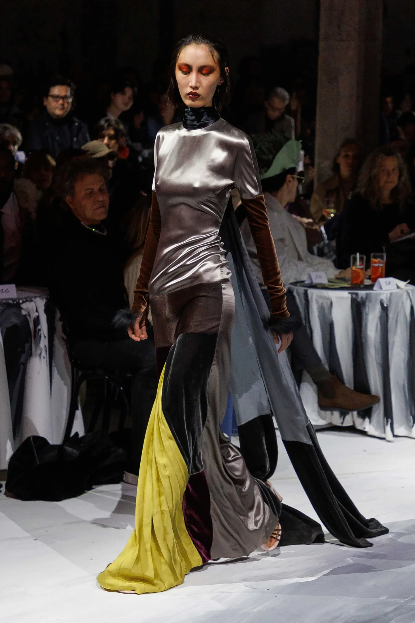 Desfile de moda com modelo vestindo traje de veludo em tons metálicos, inspirado em temas medievais.
