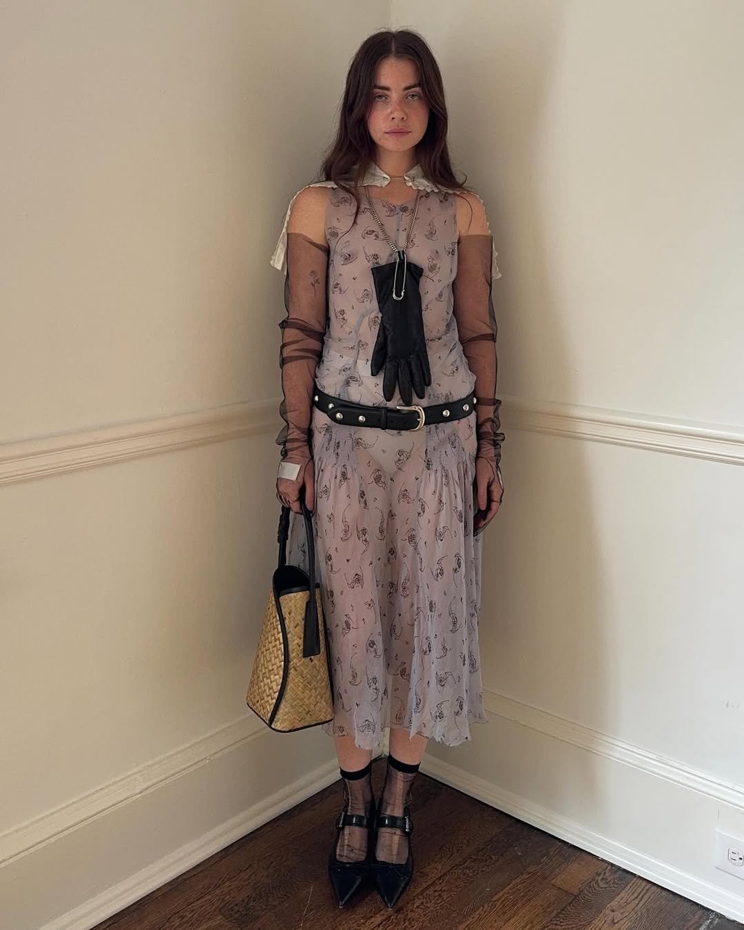 Jovem em vestido translúcido com estampa e acessórios góticos, como luvas pretas e cinto de couro, evocando um estilo medieval core.