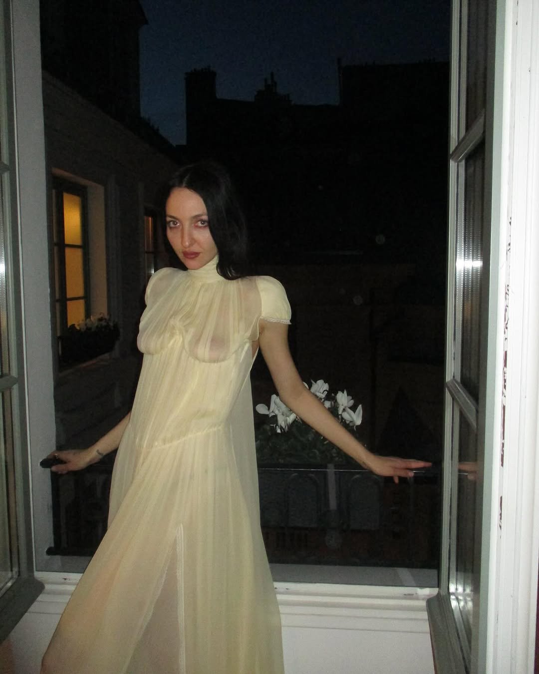 Pessoa em pé em uma varanda, vestindo um vestido leve e transparente, à noite. Medieval core