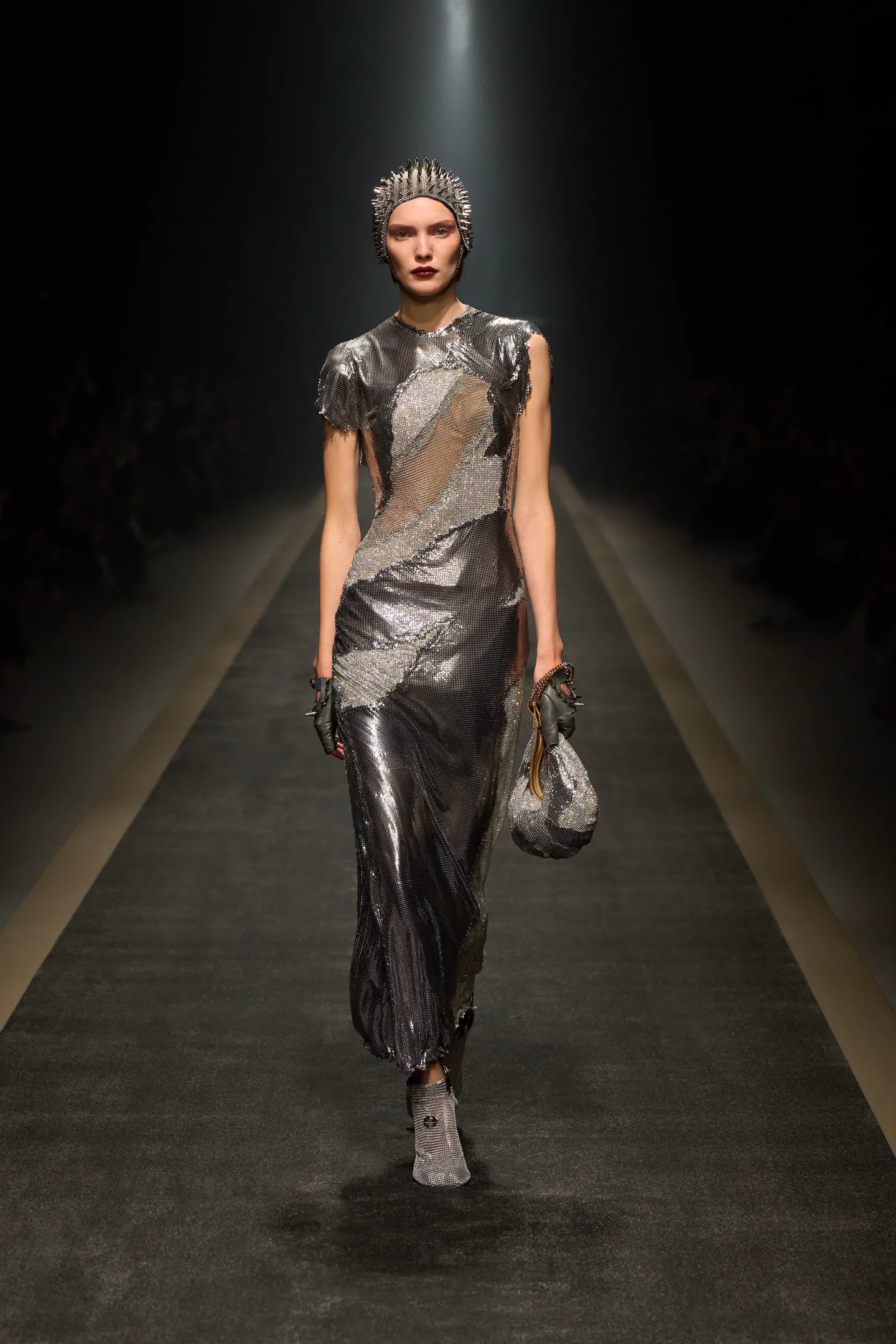 Modelo em passarela vestindo traje prateado e chapéu com pontas, evocando o estilo medieval core.