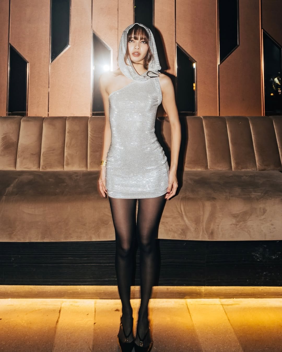 Pessoa com vestido prateado e capuz, estilo futurista, em ambiente moderno. Medieval core