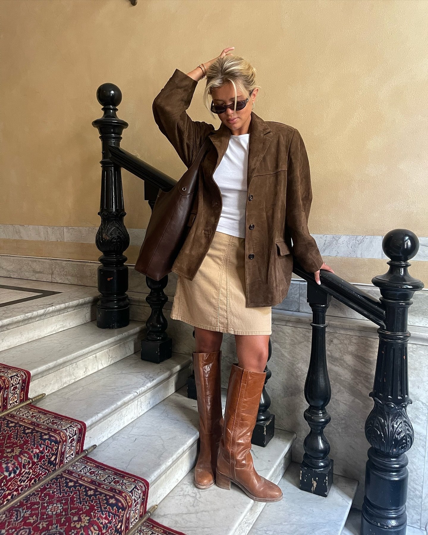 Pessoa usando casaco marrom, saia bege e botas marrons numa escada, estilo moda outono inverno 2025.