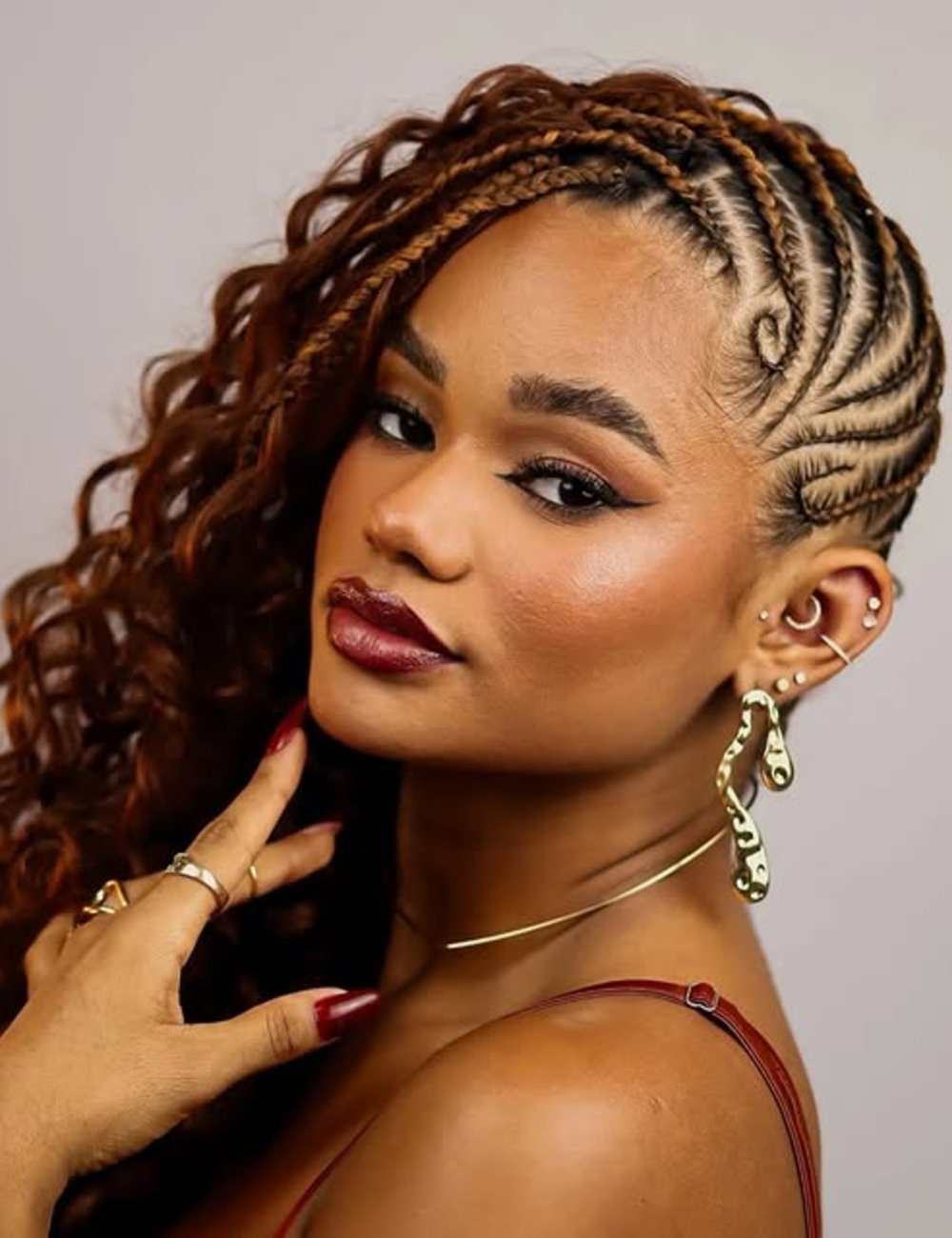 Mulher com penteado mohawk braids, cabelo trançado elaboradamente, usando brincos chamativos e maquiagem destacada.