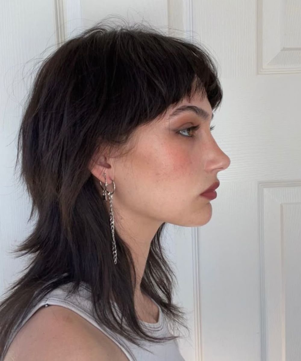 Cabelo ao estilo mullet feminino em perfil, com joias prateadas na orelha.
