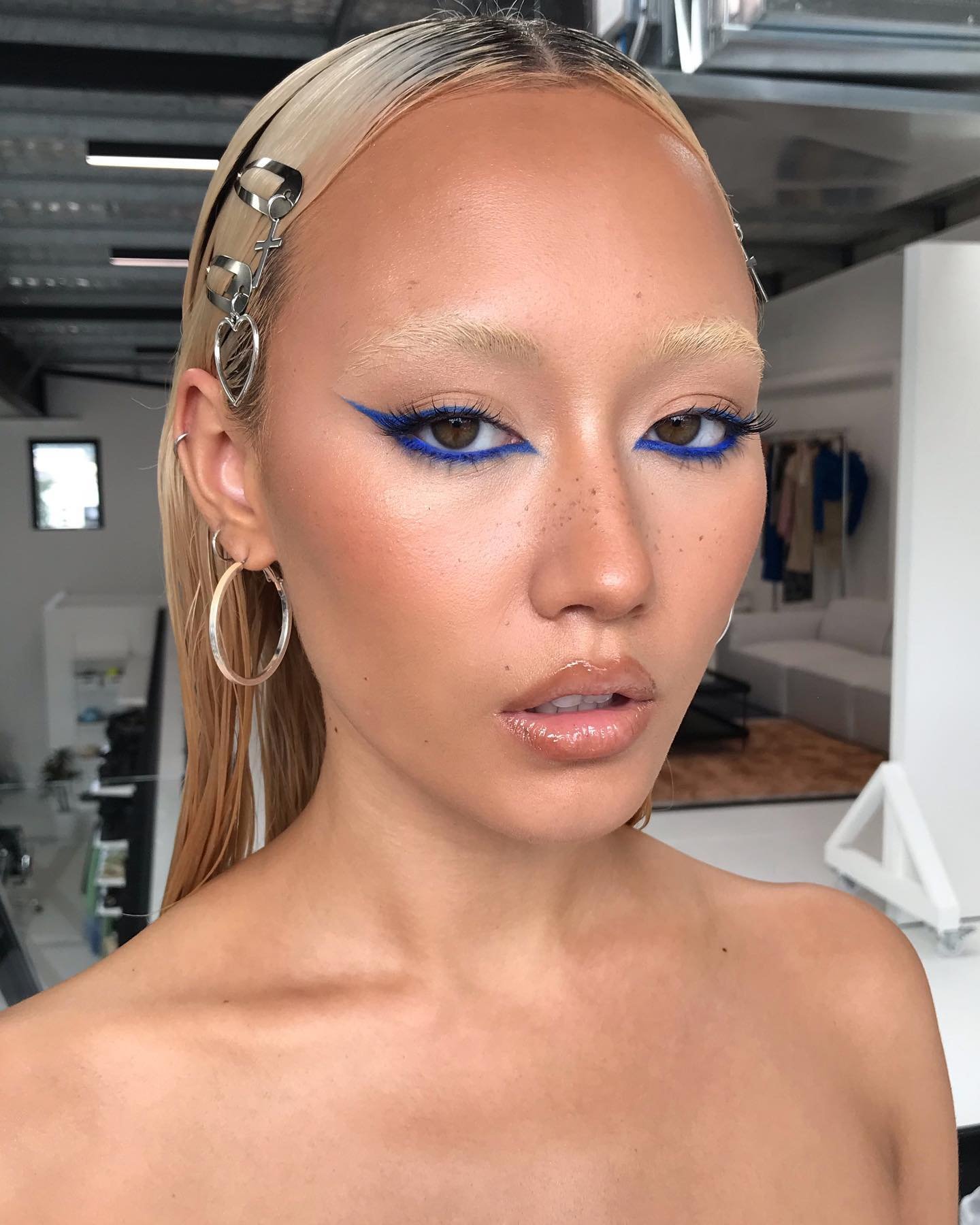 Maquiagem ousada com delineador azul, destacando olhos, efeito dos melhores lápis de olho, cabelo liso e preso com grampos.