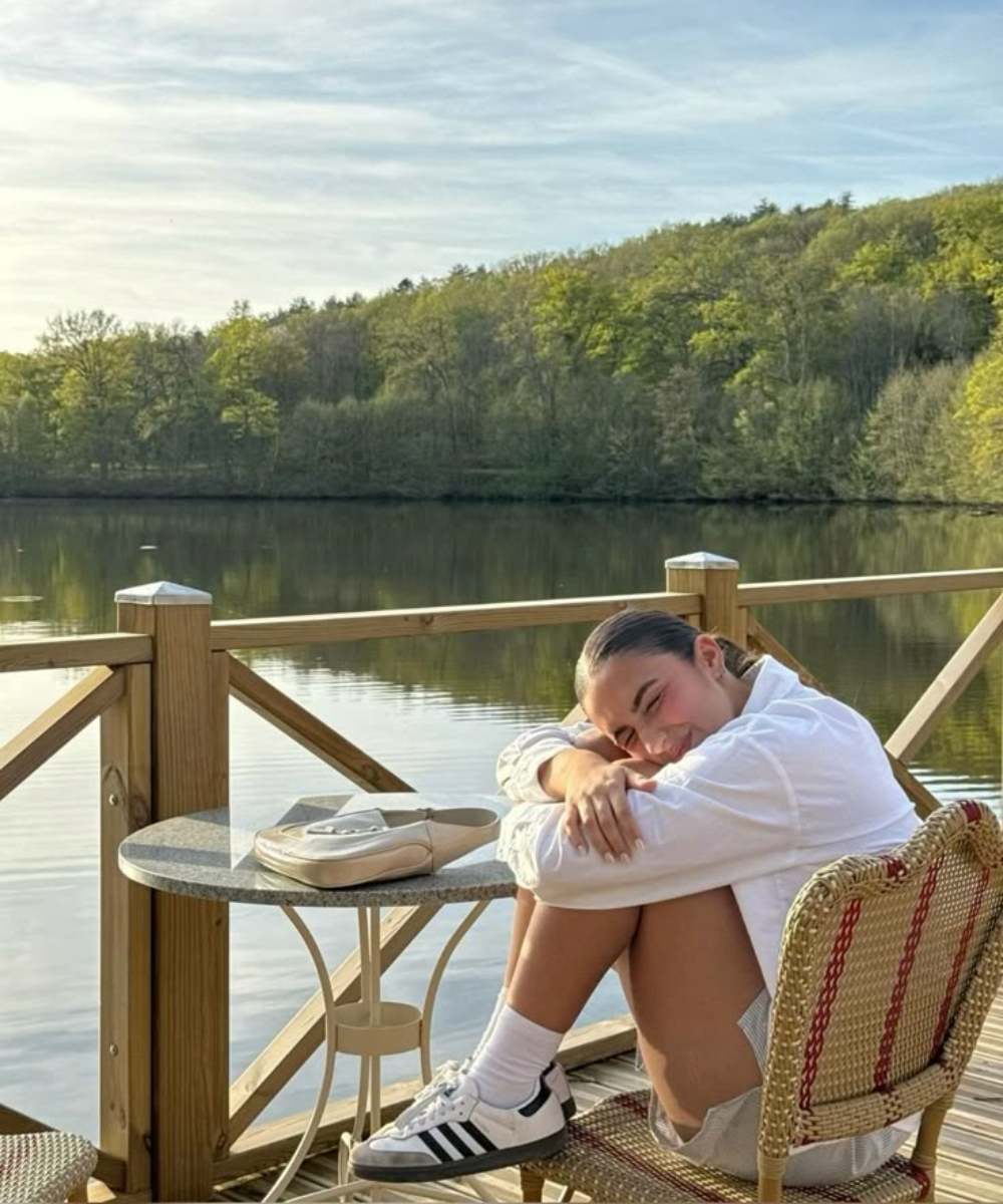 Pessoa sorrindo sentada em varanda à beira de lago. Você não está atrasada.