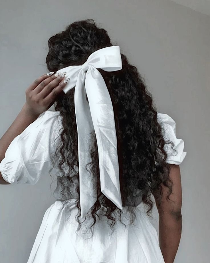 Cabelo cacheado longo adornado com um laço branco grande na parte de trás.