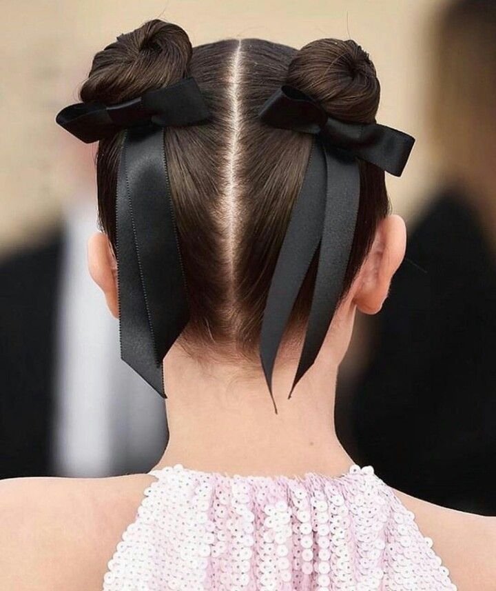 Dois coques altos adornados com laços pretos em cabelo liso dividido ao meio.