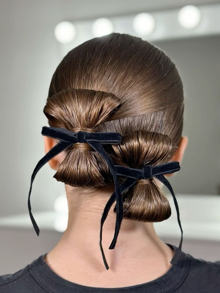Cabelo castanho em coque duplo, decorado com laços de veludo preto, criando um penteado elegante e sofisticado.
