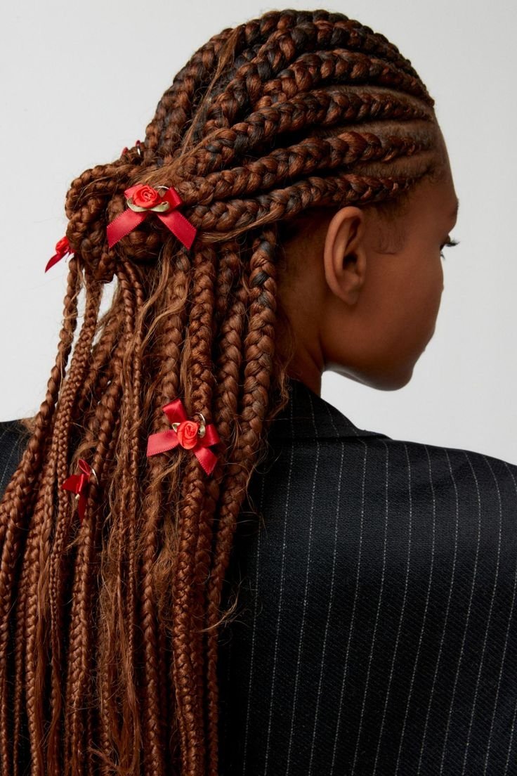 Tranças com laços vermelhos decoram o cabelo castanho em um penteado elegante e detalhado.