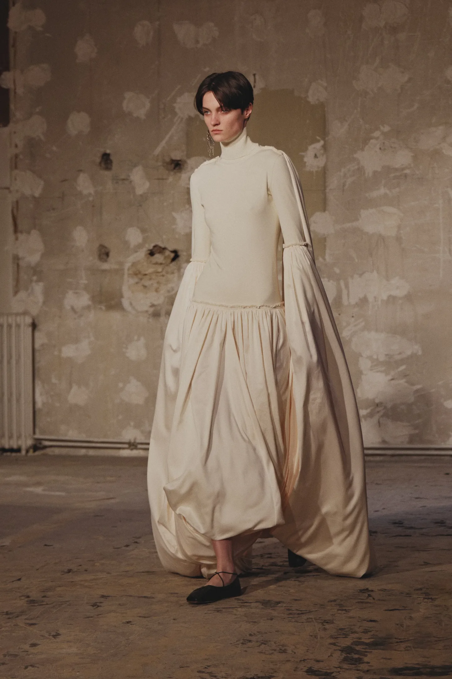 Vestido longo medieval core em cor clara, com mangas bufantes, em ambiente rústico.