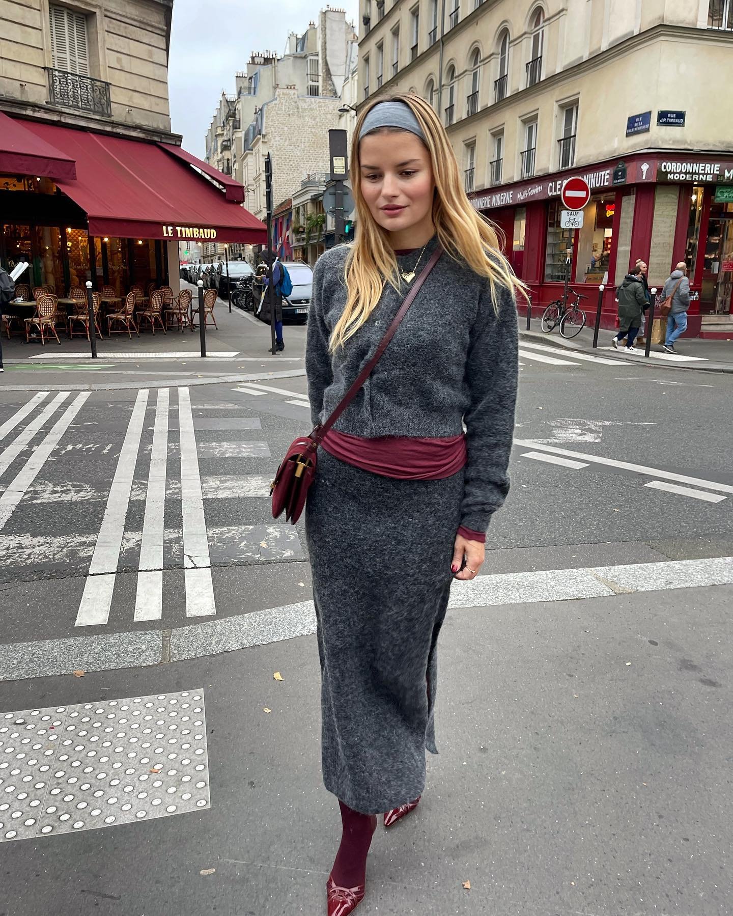 Pessoa usando roupa de frio cinza com detalhes bordô, cruzando uma rua em Paris.