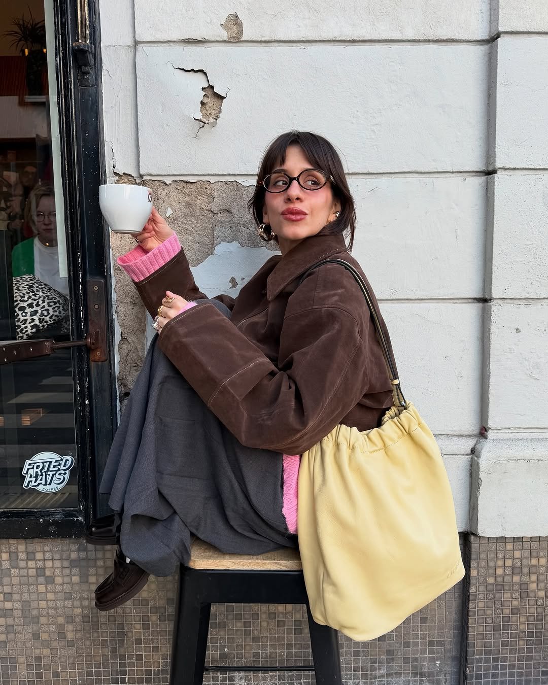 influenciadora com look marrom usando óculos ovais pequenos, uma das armações de grau estilosa