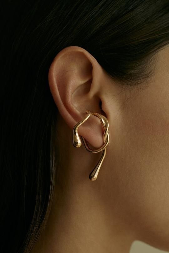 Brinco dourado com design fluido em orelha feminina, refletindo tendências de estilo moderno.
